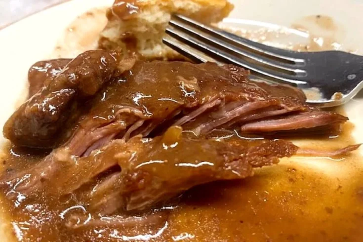 Fork-tender baked steak covered in rich brown gravy, showing juicy, fall-apart beef and classic homemade comfort food flavor