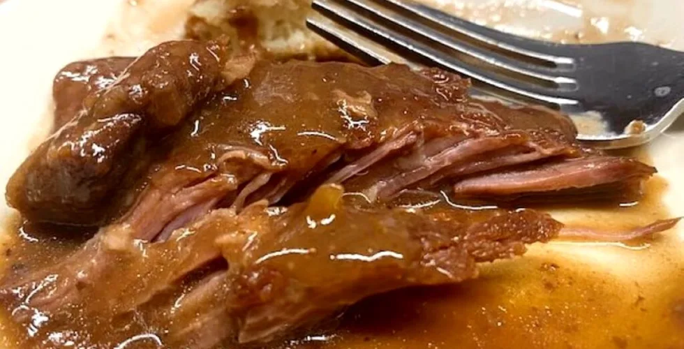 Fork-tender baked steak covered in rich brown gravy, showing juicy, fall-apart beef and classic homemade comfort food flavor
