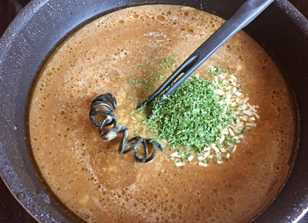 Savory brown gravy mixture simmering in a saucepan with onion flakes and parsley, whisked smooth for baked steak