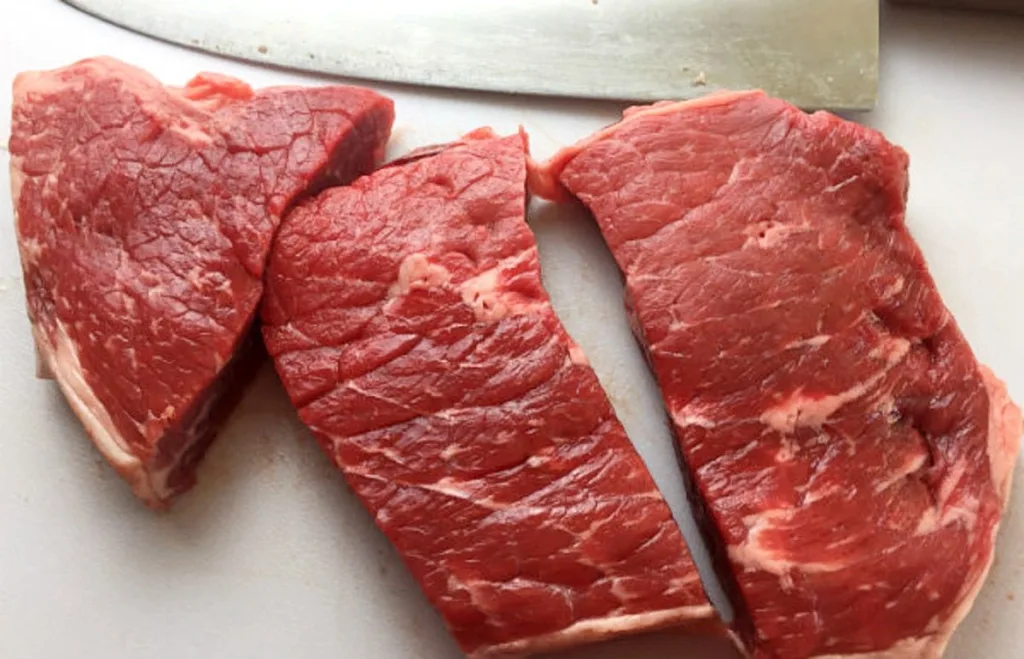 Raw round steak pieces on a cutting board, ready to be seasoned and browned for baked steak