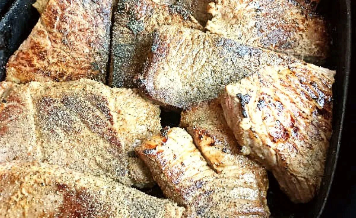 Browned pieces of steak layered snugly in a roasting pan, slightly overlapping or ‘shingled’ before baking