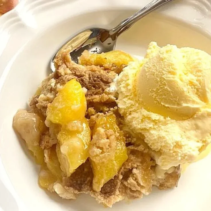 fresh peach cobbler in a bowl with ice cream.