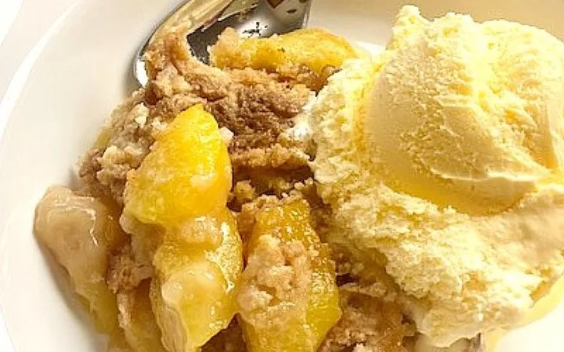 fresh peach cobbler in a bowl with ice cream.