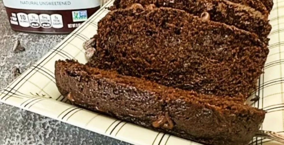 A loaf of chocolate chip zucchini bread on a platter. A can of Hershey's cocoa is next to it.