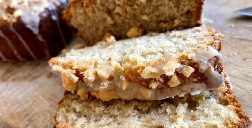 Slices of homemade peanut butter banana bread with a crunchy peanut topping on a wooden cutting board.