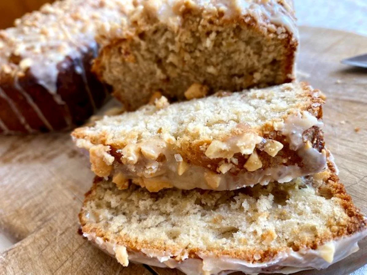 Slices of homemade peanut butter banana bread with a crunchy peanut topping on a wooden cutting board.