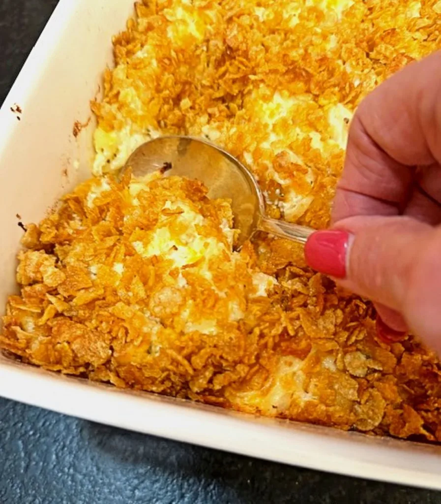 dishing up a spoonful of buttery, cheesy funeral potaoes with crisp, buttery cornflake topping