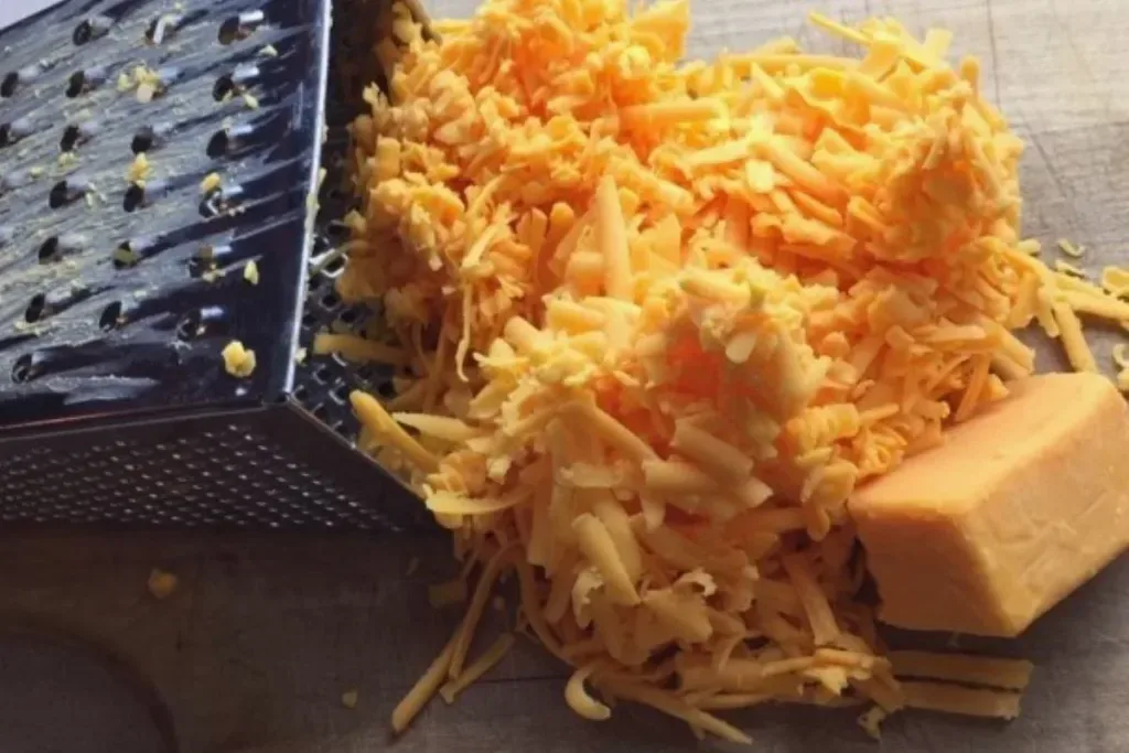 grating cheddar cheese from a block with an ordinary box grater