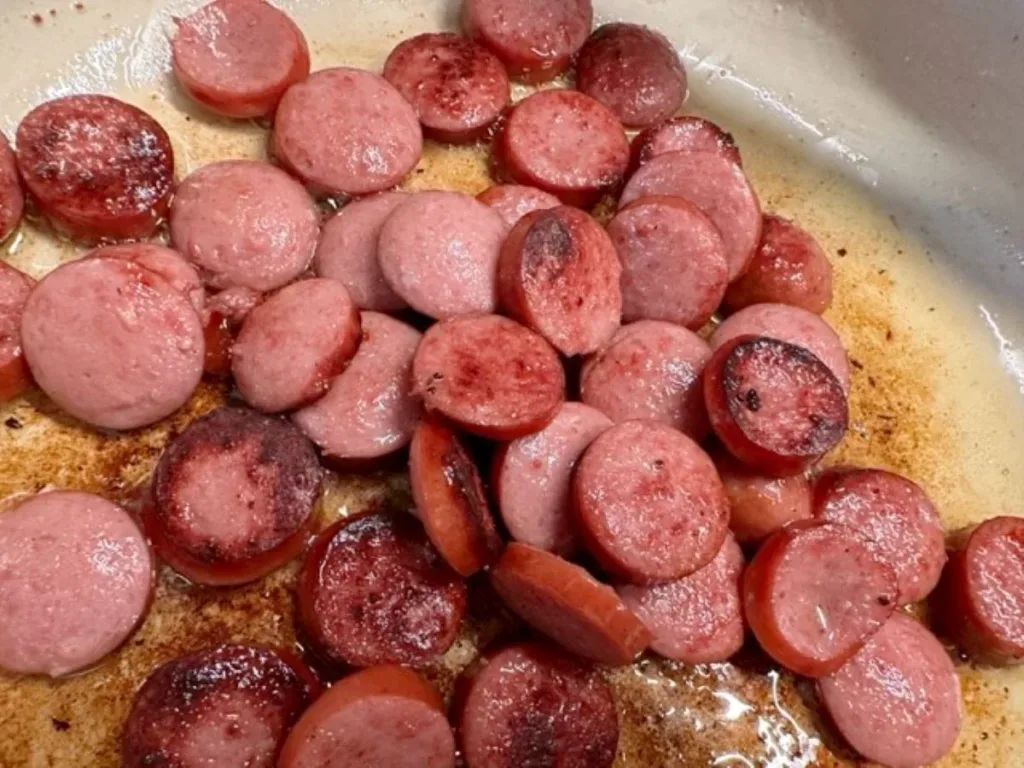 thinly sliced sausage browning in a skillet